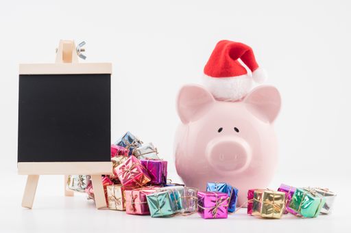 A piggy bank in a Santa Claus hat, chalkboard, and colorful gift boxes on the white background, the concept of budgeting for the festive season