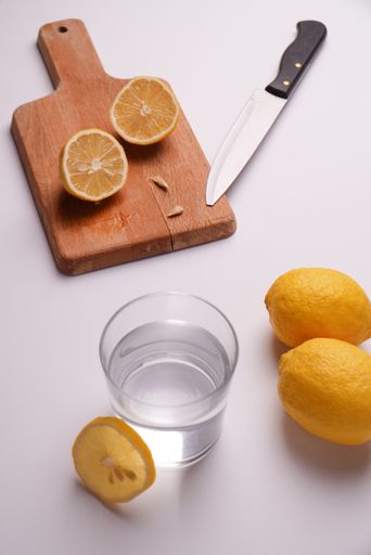 A verti shot of sliced lemon on a wooden board with a glass of water for making a refreshing drink