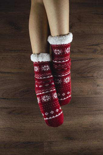 A top view shot of crossed female legs demonstrating red Christmas socks on the wooden floor background