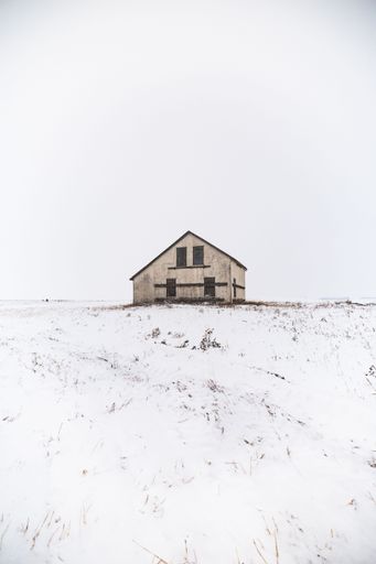 A picturesque two-story house sits atop a snow-covered hill, overlooking the surrounding landscape