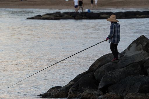 A woman standing on the coastal rock and catching fish with a fishing rod