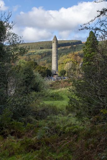 A vertical shot of a concrete lighthouse surrounded by green trees and high mountains