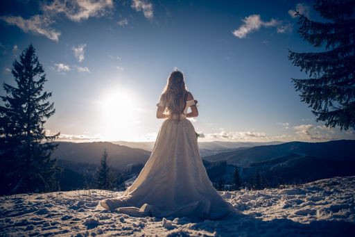 A back view of Caucasian woman wearing wedding drees and standing on snow covered field