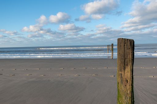 A cloudy sky over a sandy empty beach with wooden poles and a wavy seascape view in Norderney, Germany