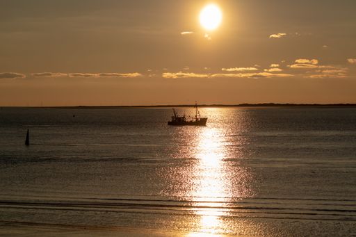 A majestic shot of a brightly shining sunset sun with a reflection on calm seawater in Norderney, Germany
