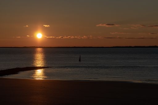 A majestic shot of a brightly shining sunset sun with a reflection on calm seawater in Norderney, Germany