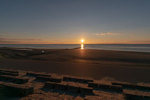 A calm seascape view and a sandy beach with a setting down sunset sun on the horizon in Norderney, Germany