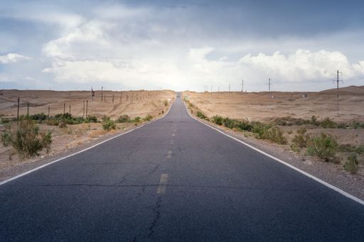 A rural road winds across a vast landscape of rolling hills and fields, stretching towards the horizon