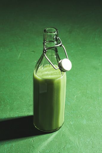 A vertical shot of a green smoothie in a glass bottle on a green surface