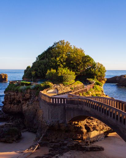 A vertical shot of a beautiful bridge on a cliff covered in green vegetation. Biarritz, France.