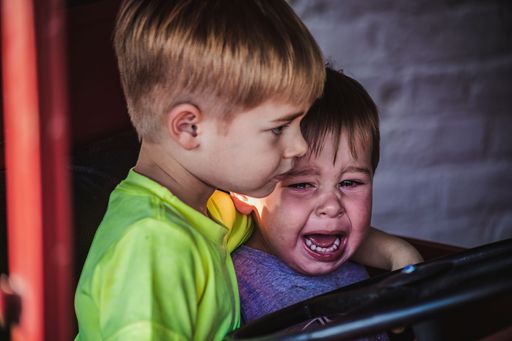An adorable older brother comforting his crying younger toddler brother