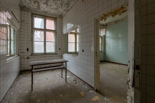 An empty decaying room with a table and torn ceramic walls in an abandoned place