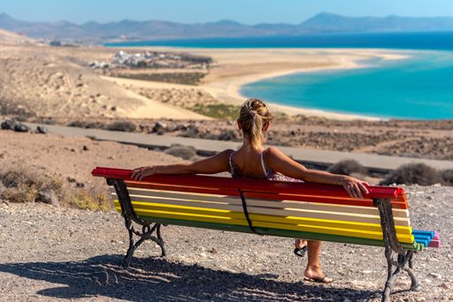 A young woman sitting on a colorful bench with a view of the Sotavento Beach in Spain