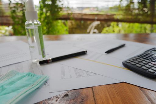 A closeup shot of the medical mask, calculator, antiseptic, papers, and a pen on the wooden table