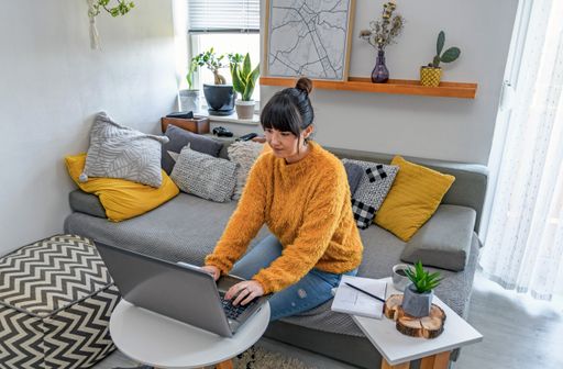 A shallow focus closeup of a female using her laptop while sitting on the sofa in the living room