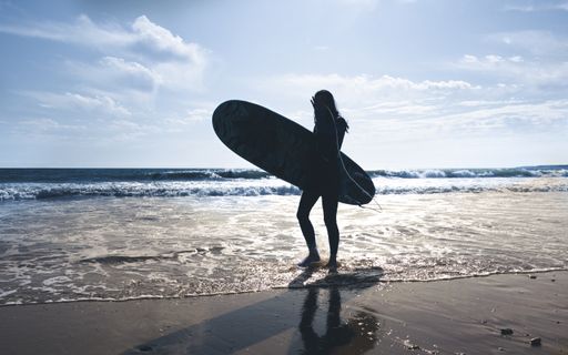 A surfer standing at the beach holding a surfing board getting ready to take over the ocean