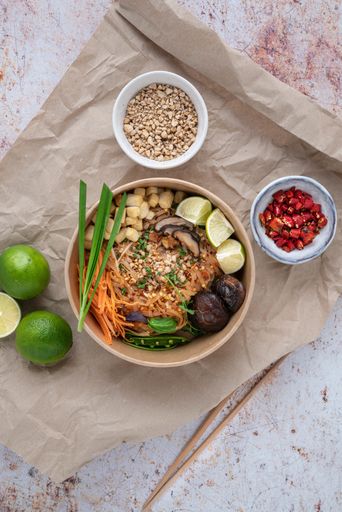 A vertical shot of a serving of delicious noodles with salads, lime, greens, buckwheat, and crumbs