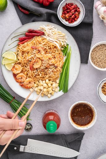 A vertical shot of a serving of delicious noodles with salads, lime, greens, shrimps, and crumbs