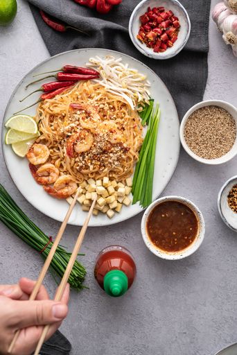 A vertical shot of a serving of delicious noodles with salads, lime, greens, shrimps, and crumbs