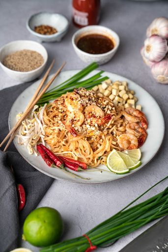 A vertical shot of a serving of delicious noodles with salads, lime, greens, shrimps, and crumbs