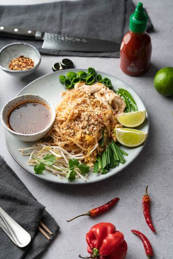 A vertical shot of a serving of delicious noodles with salads, lime, greens, sauce, and crumbs