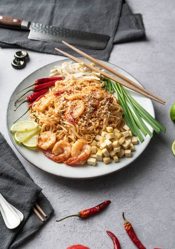 A vertical shot of a serving of delicious noodles with salads, lime, greens, shrimps, and crumbs