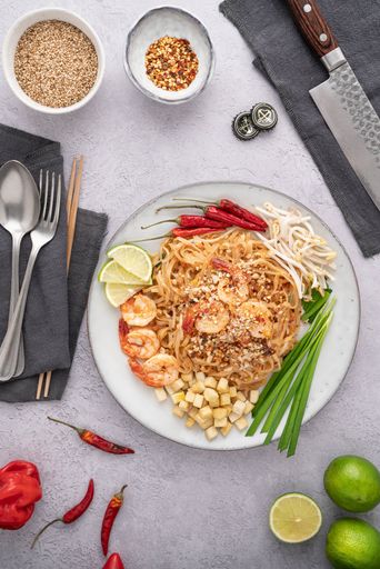 A vertical shot of a serving of delicious noodles with salads, lime, greens, shrimps, and crumbs