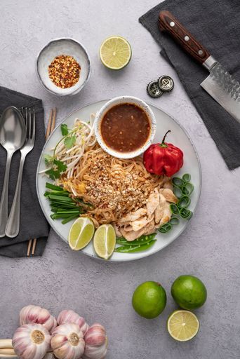A vertical shot of a serving of delicious noodles with salads, lime, greens, sauce, and pepper