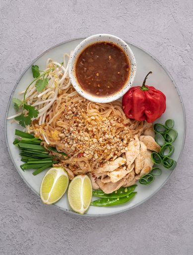 A vertical shot of a serving of delicious noodles with salads, lime, greens, sauce, and pepper