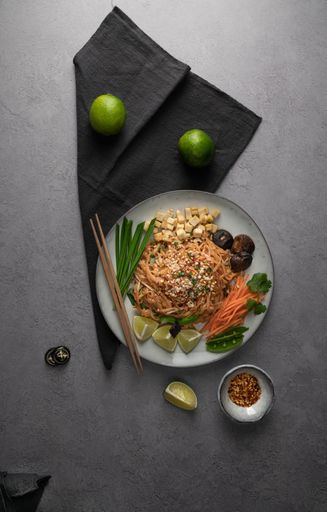 A vertical shot of a serving of delicious noodles with salad, lime, greens, carrot, and crumbs