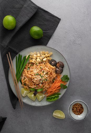 A vertical shot of a serving of delicious noodles with salad, lime, greens, carrot, and crumbs