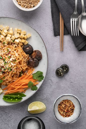 A vertical shot of a serving of delicious noodles with salad, lime, greens, carrot, and crumbs