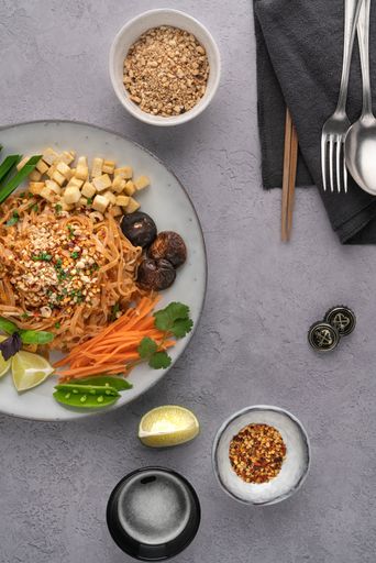 A vertical shot of a serving of delicious noodles with salad, lime, greens, carrot, and crumbs