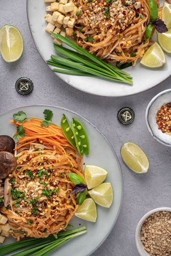 A vertical shot of servings of delicious noodles with salad, lime, greens, carrot, and crumbs