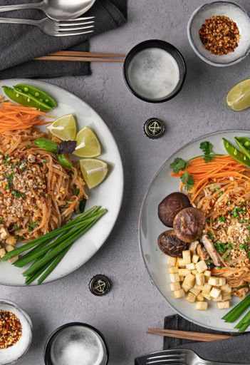 A vertical shot of servings of delicious noodles with salad, lime, greens, carrot, and crumbs