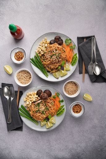 A vertical shot of servings of delicious noodles with salad, lime, greens, carrot, and crumbs