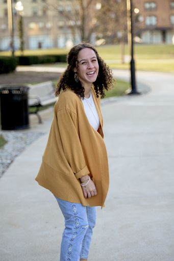 A woman with curly hair wearing a yellow jacket in a park under sunlight with a blurry background