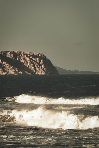 A vertical shot of foam waves breaking near the rocky seacoast