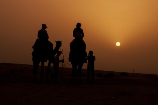 The silhouette of people on the camel against the orange sky in a desert