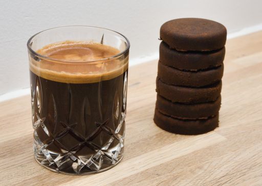 A closeup of a cup of coffee with 6 espresso shots and the 6 espresso pucks on the side used for a tiramisu recipe