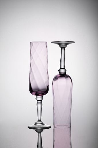 A shot of two empty pink champagne glasses on the white surface with shadows, one is upside down