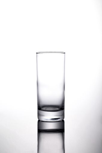 A vertical shot of an empty highball glass on the white surface with a shadow