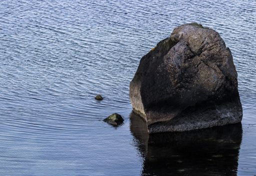 A big rock and two small rocks in the middle of the calm water of the sea