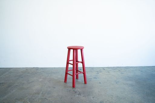 A vibrant red stool on the hardwood floor in a modern interior against a white wall