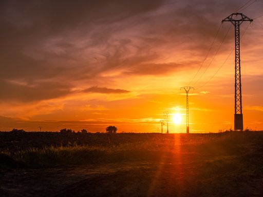 A beautiful shot of a sunset in the open green field with power lines under the cloudy sky