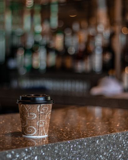 A vertical selective focus shot of a coffee paper cup on the bar