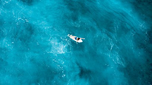 A girl laying on a surfboard and floating in the open sea with crystal clear water in Maldives