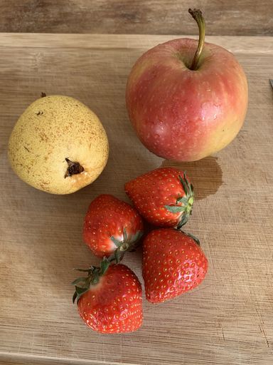 A vertical shot of strawberries and apples on a cutting board