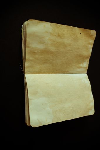 A vertical shot of an old weathered blank paper diary notebook isolated on a black background