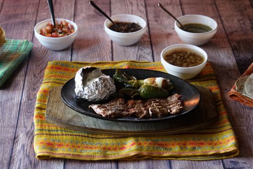 A closeup shot of flank steak and cabreria with salads and sauce on the wooden table